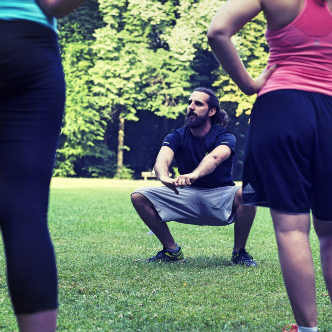 Personal Trainer macht beim everfits Outdoor Training die Kniebeuge vor Personal Trainer macht beim everfits Outdoor Training die Kniebeuge vor